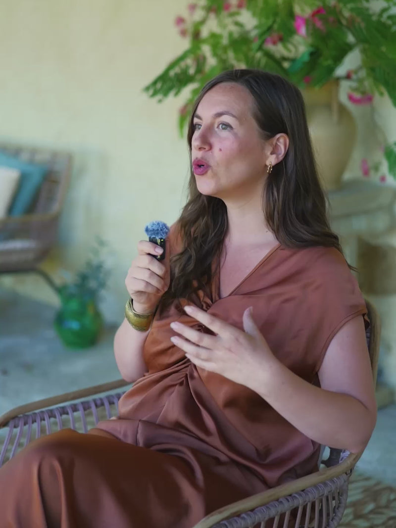 Femme qui parle face à la caméra sur sa terrasse, petit micro en main, arrière plan avec une plante
